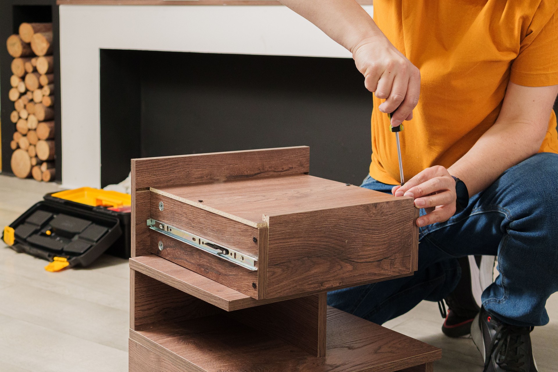 A man in an orange shirt is working on a piece of furniture